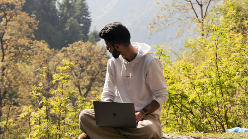 A young man sitting in nature with his laptop